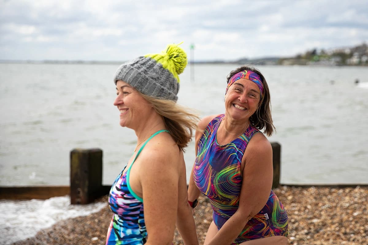 Three friends laughing together on the shore after an open-water swim