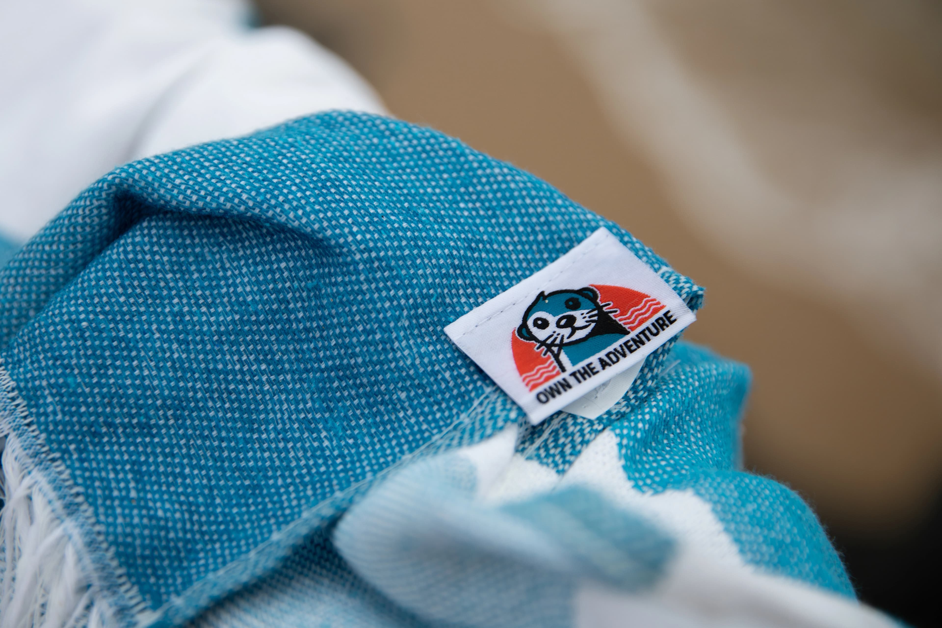 Own The Adventure woven label on a colourful striped towel